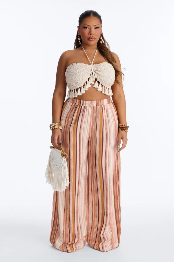 Woman models a cream crochet halter top with tassels and striped wide-leg pants. Perfect plus-size boho summer fashion for new collection.