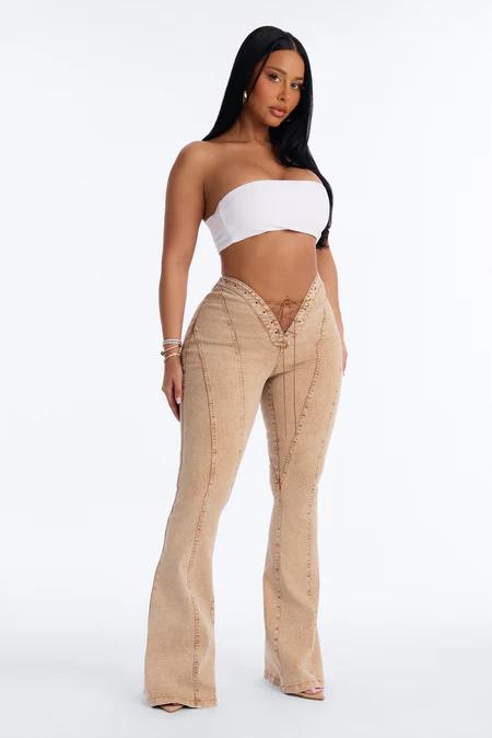 Woman in a white strapless crop top and high-waisted, lace-up beige flare jeans. She stands on a white background, looking forward.