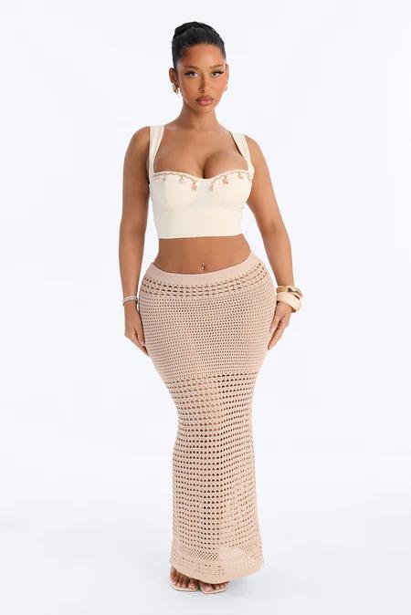 Toma de cuerpo entero de una mujer de pie, vistiendo un crop top bustier bordado blanco roto y una falda maxi de croché beige de talle alto.