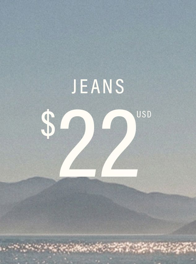 Paisaje montañoso azul brumoso con agua brillante, con texto blanco: 'JEANS $22 USD'. Compra jeans de mezclilla asequibles.
