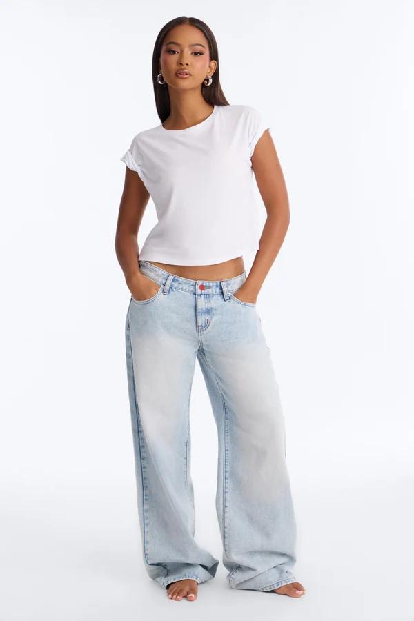Modelo posa con camiseta blanca básica y jeans anchos de lavado claro sobre fondo blanco, destacando una colección de moda urbana casual.