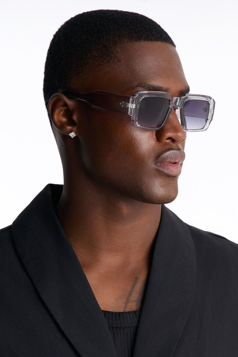 Stylish man in black blazer, wearing trendy clear gray square sunglasses with dark lenses, highlighting new eyewear collection.