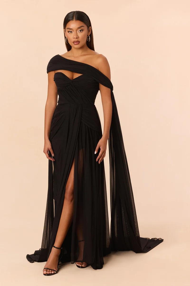 Elegant black evening gown featuring a draped one-shoulder neckline, high leg slit, and flowing cape details from the formalwear collection.