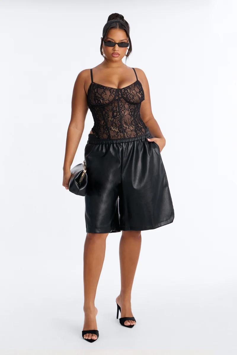 Chic woman in a black lace corset bodysuit and baggy faux leather shorts posing with a clutch, showcasing a trendy night-out outfit.