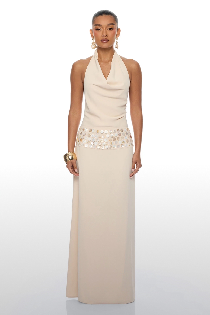 Elegante vestido de noche color crema con cuello halter, cintura de lentejuelas y accesorios dorados, de la nueva colección formal.