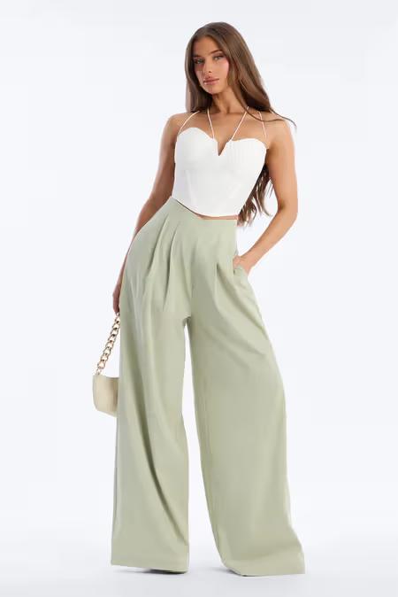 Mujer con estilo en top corsé halter blanco, pantalones plisados anchos verde salvia y bolso cadena.