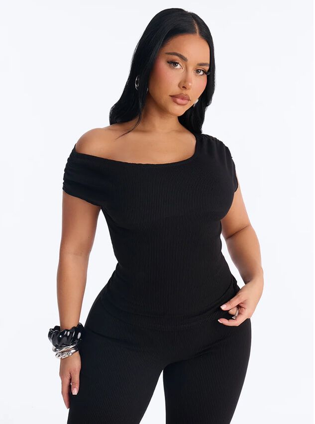Woman posing in a chic black ribbed off-the-shoulder top and matching trousers from a casual loungewear collection against a white background.
