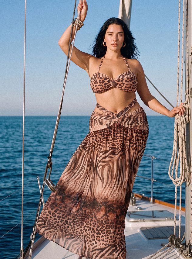 Stylish woman in a tan leopard print bikini and sheer sarong on a boat, showcasing chic swimwear for resort wear.