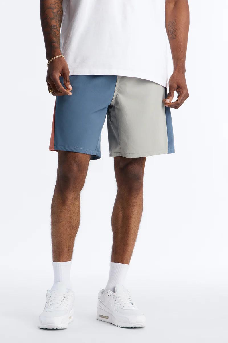 Man models stylish color-block shorts in blue, light grey, and orange, paired with a white tee. Ideal for men's summer athletic fashion.
