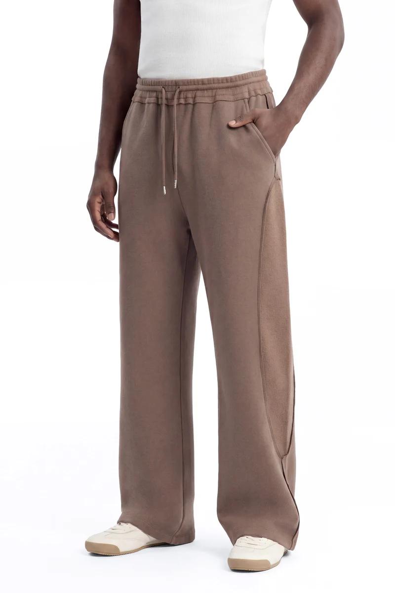 Brown wide-leg drawstring sweatpants with unique side paneling, worn by a model, highlight relaxed comfort and modern casual style. New loungewear.