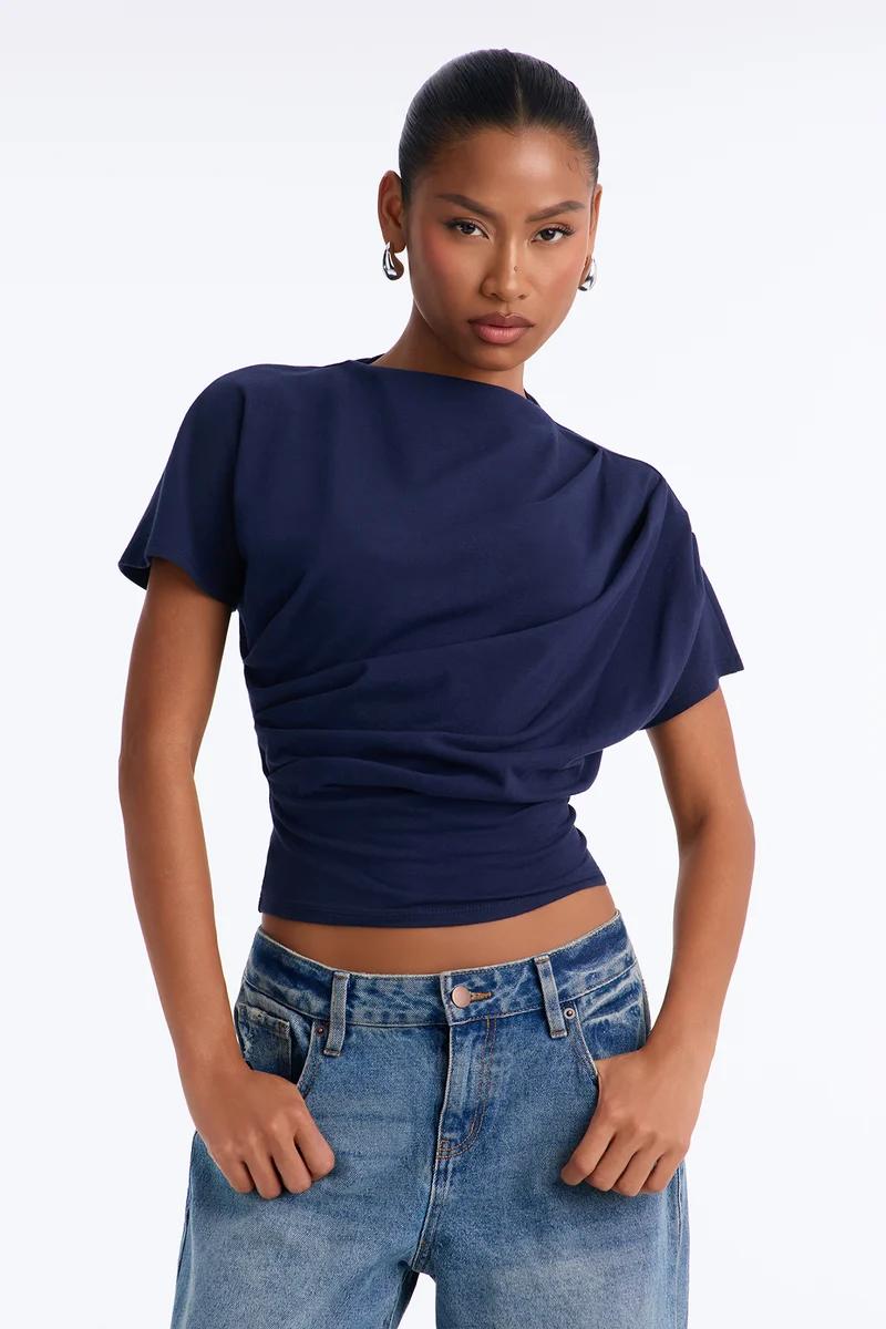 Woman wearing a navy blue draped short-sleeve top and blue jeans.