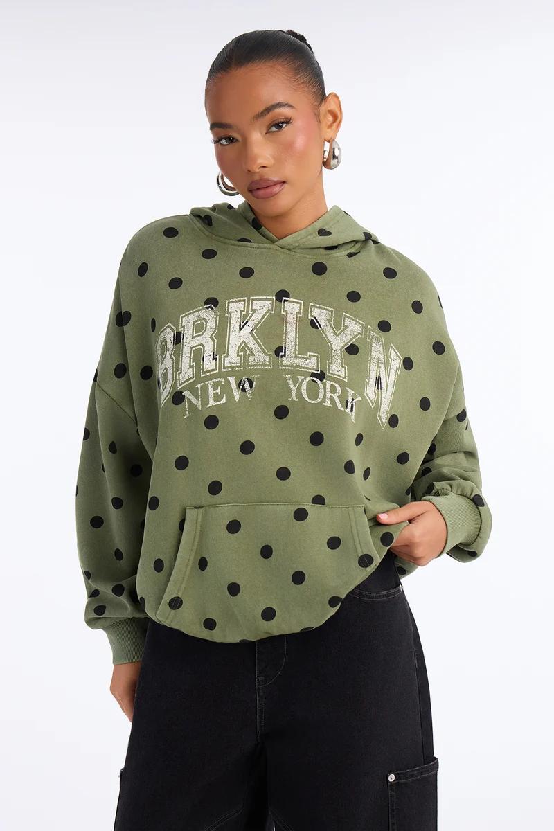 Woman wearing an olive green polka dot hoodie with Brooklyn New York print.
