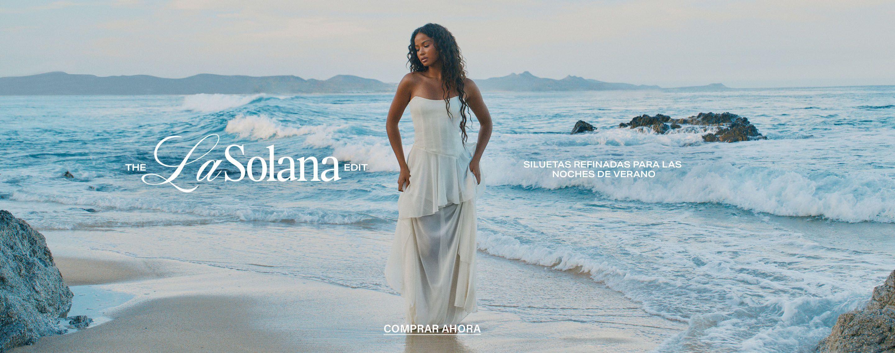 Modelo con vestido blanco fluido de La Solana Edit en la playa. Siluetas refinadas para noches de verano. ¡Compra ahora!