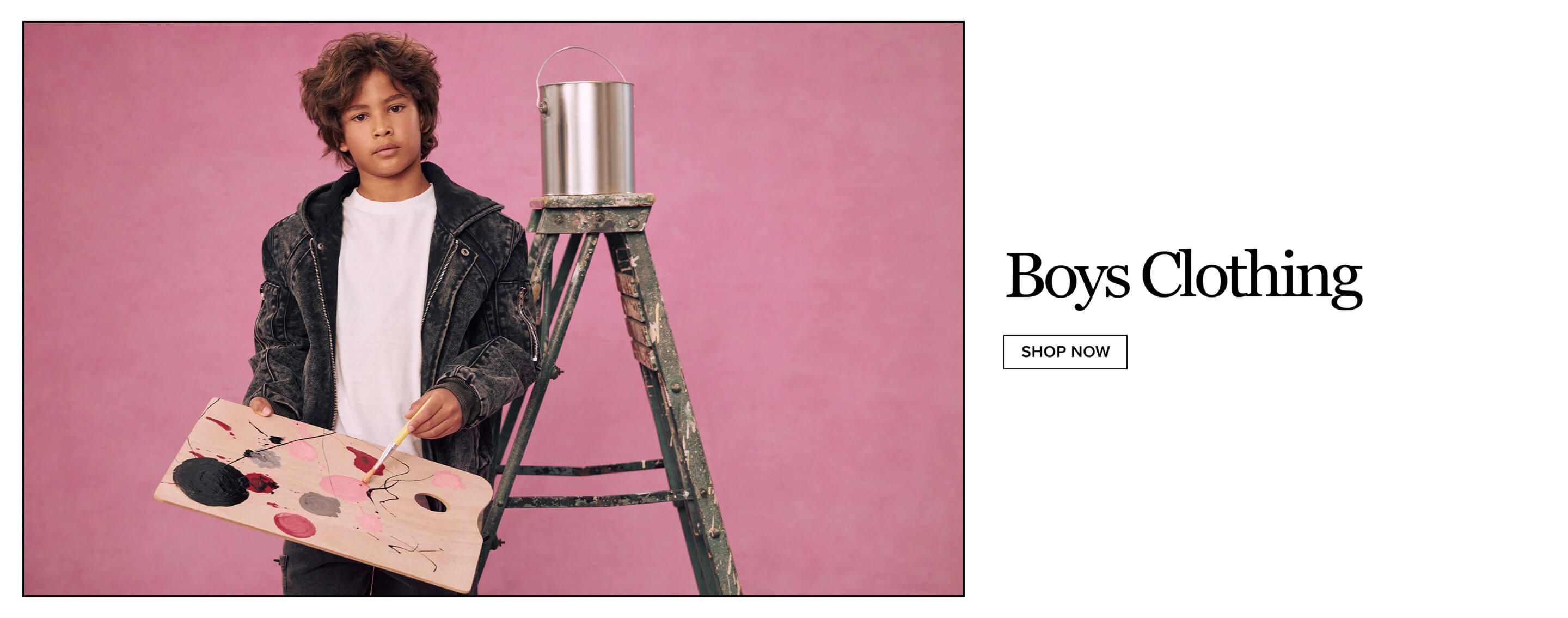 Boy in a dark denim jacket and white t-shirt holds a wooden paint palette next to a green ladder and metal paint can on a pink background.