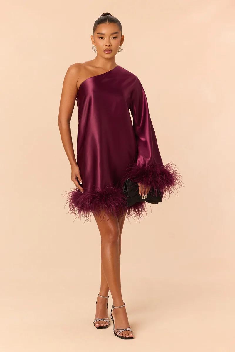 Model wearing a plum satin one-shoulder mini dress with feather trim, showcasing elegant holiday party wear and evening dress trends.