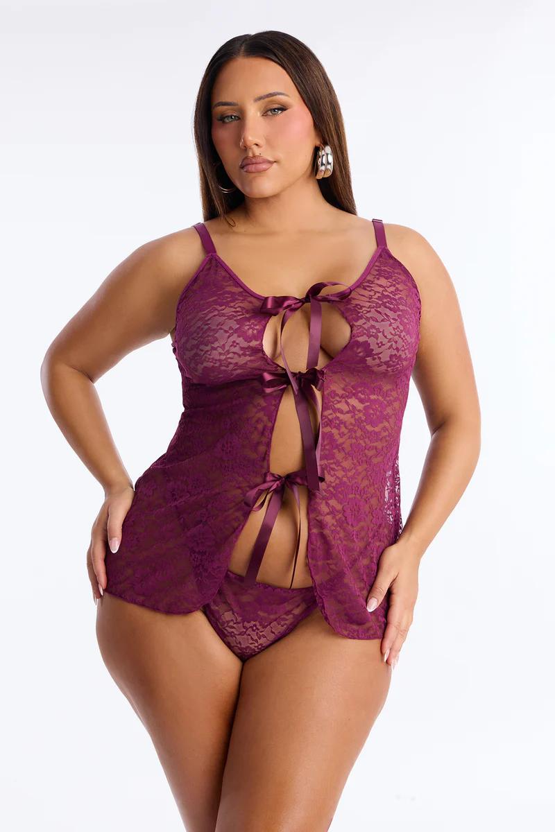 Full-figured woman in a dark plum lace babydoll lingerie set with satin ties, showcasing new intimate apparel.