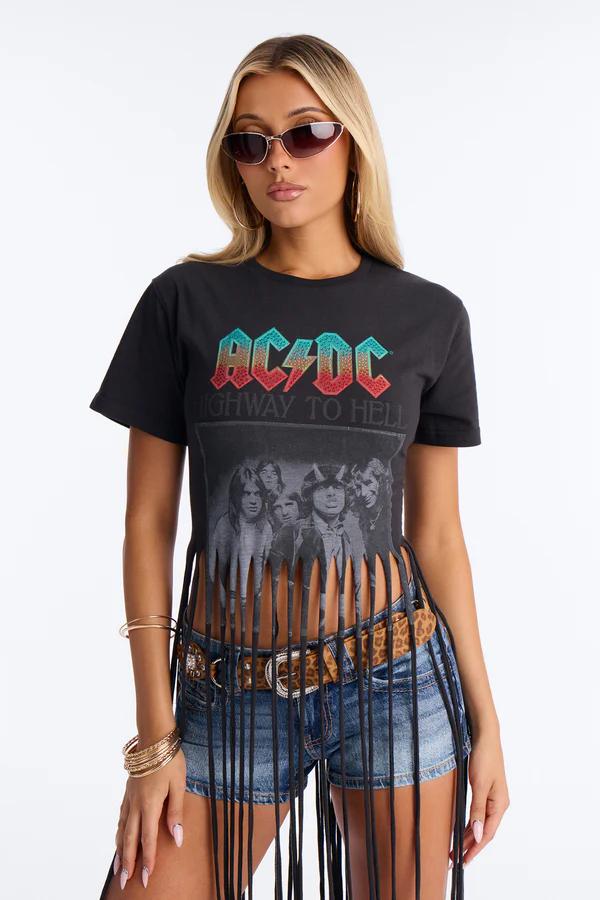 Blonde woman in cat-eye sunglasses and a fringed black AC/DC 'Highway to Hell' tee, denim shorts, leopard belt, and gold bracelets.
