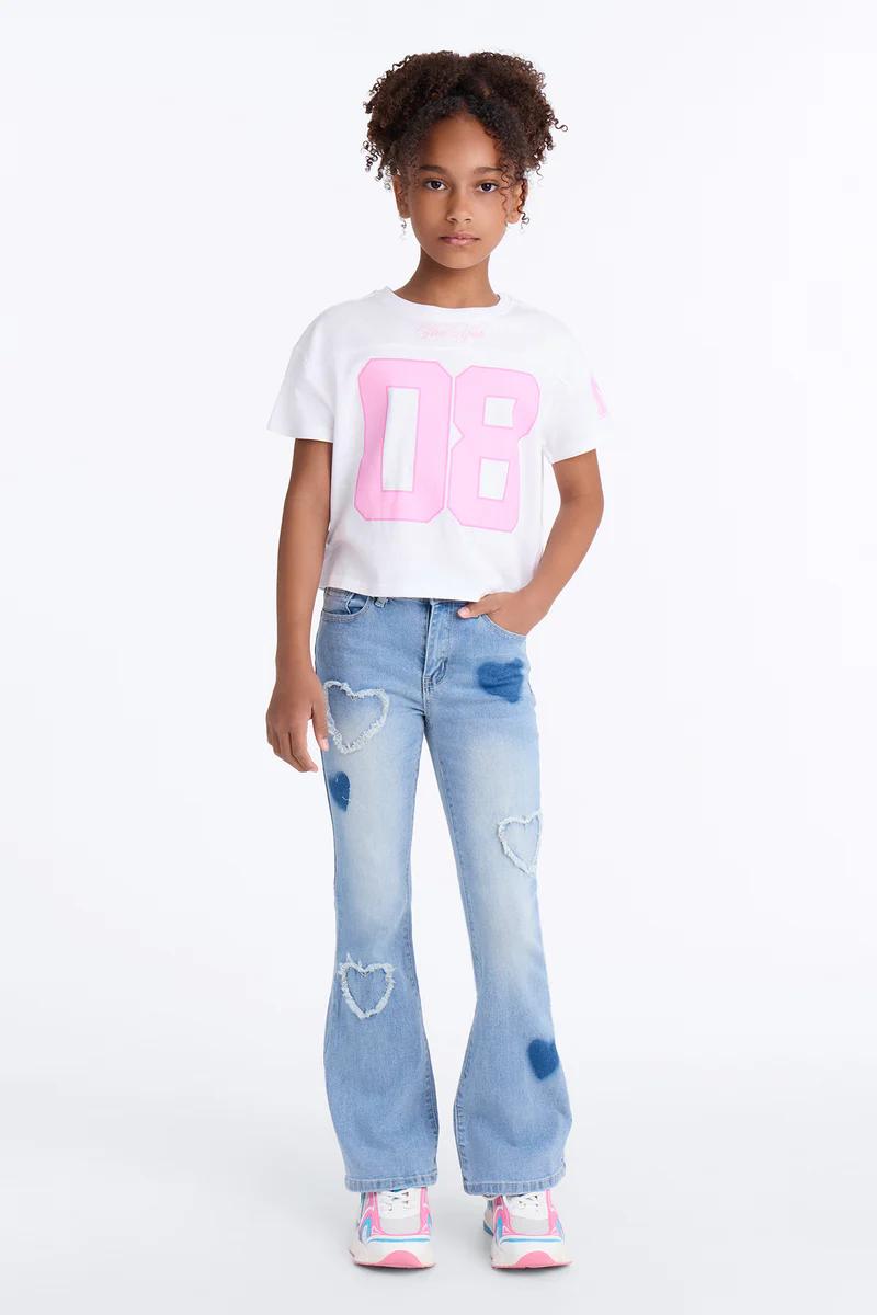 Niña con camiseta blanca 08, vaqueros acampanados lavado claro con corazones y zapatillas rosas. Moda infantil casual y elegante.