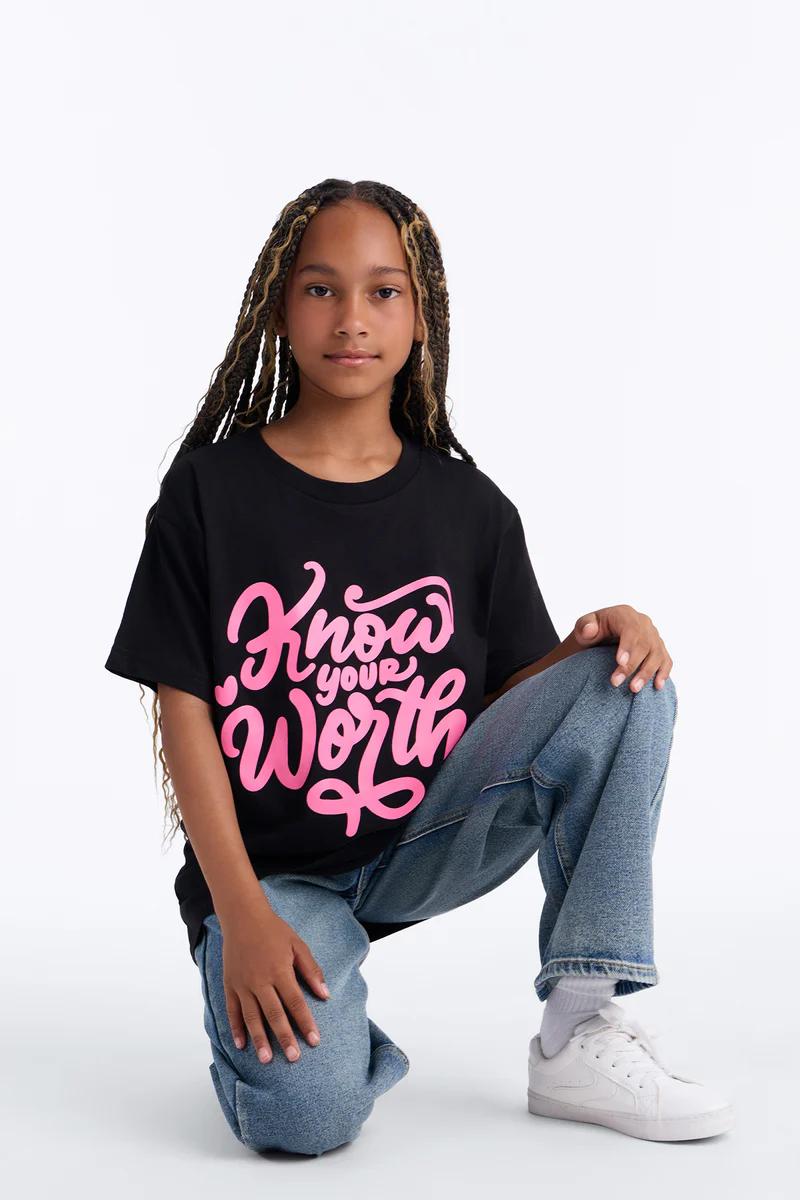 Girl with braids in black "Know Your Worth" tee, blue jeans & white sneakers. Empowering.