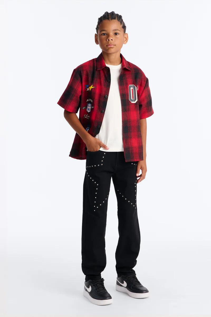 Stylish boy wears red plaid shirt, white tee, black studded pants. Youth fashion.