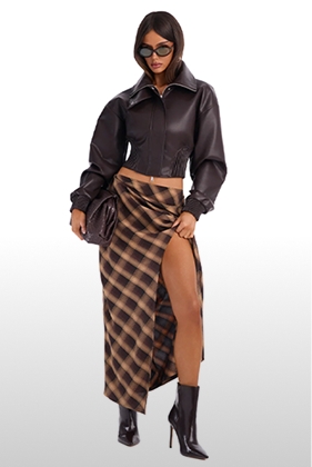 Model poses in a dark brown leather bomber jacket and brown plaid high-slit maxi skirt for a trendy autumn fashion collection catalog.