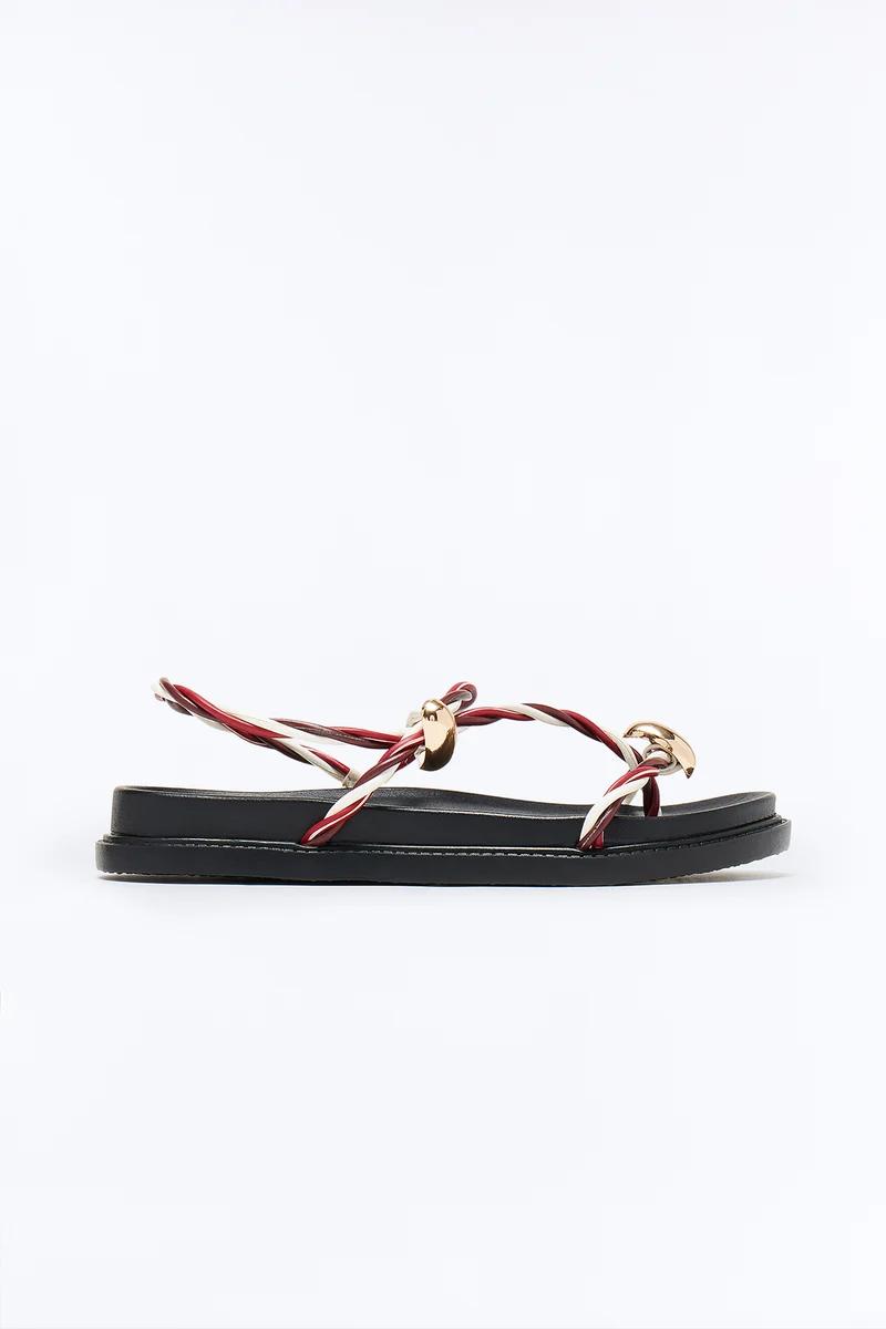 Black flat sandal with red and white twisted cord straps and gold metal accents.