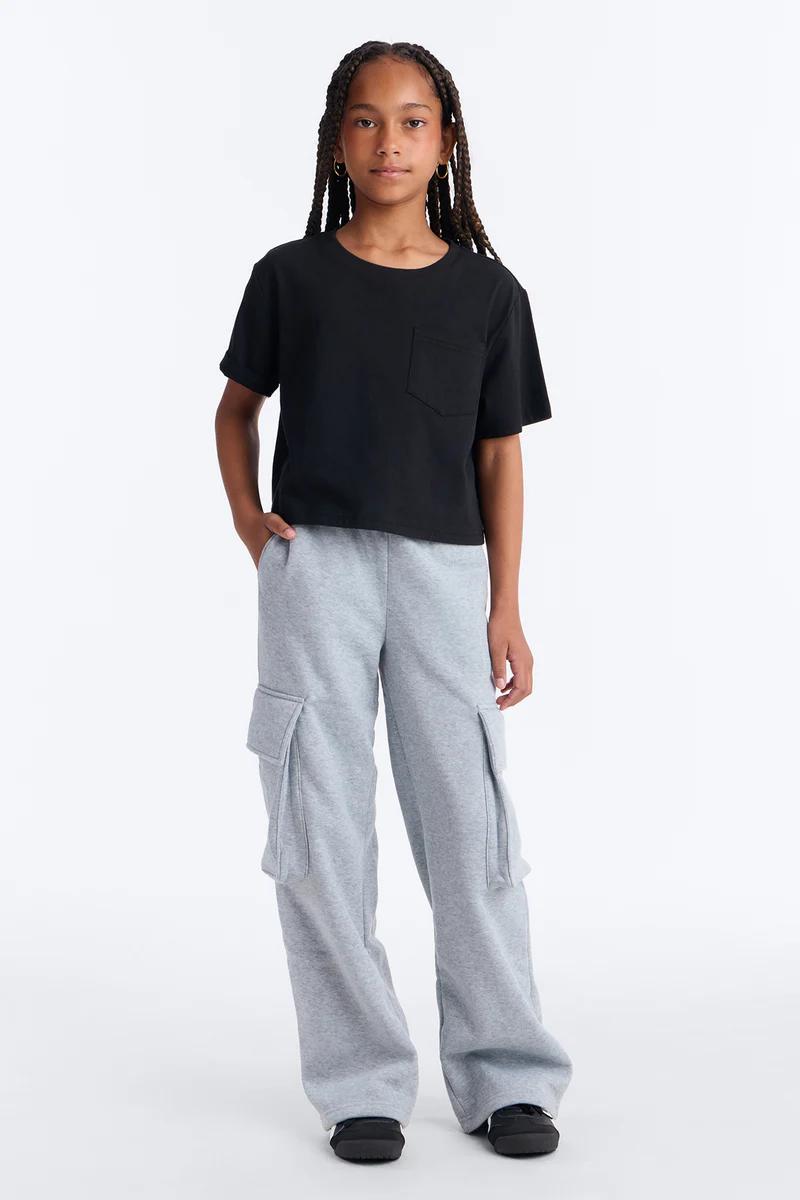 Young girl wearing a black pocket t-shirt and grey wide-leg cargo sweatpants.