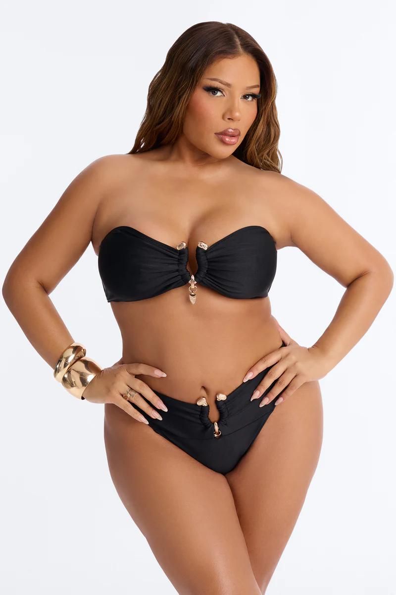 Woman in a black strapless bikini with gold hardware, hands on hips, showcasing a trendy plus size swimwear style.