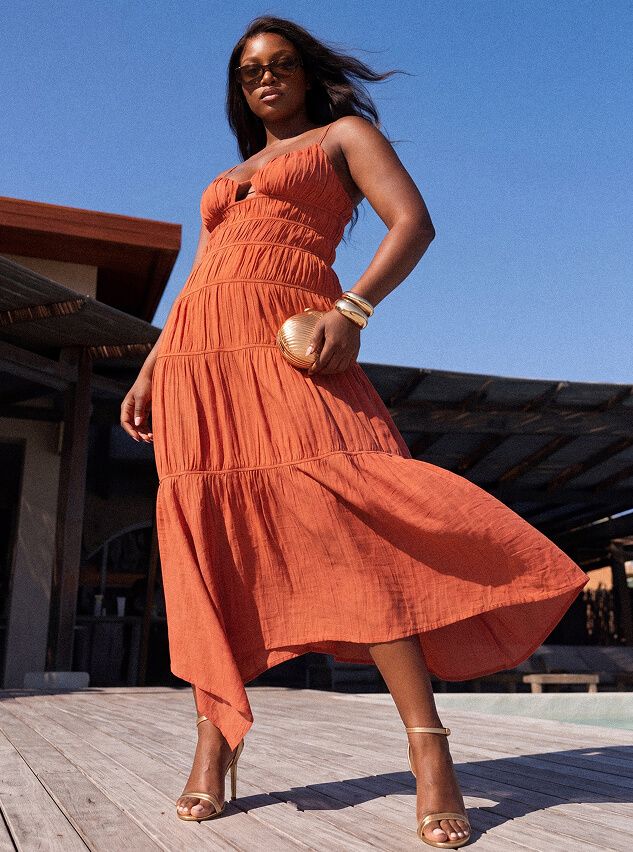 Mujer con vestido midi escalonado terracota, accesorios dorados, sandalias y bolso. Ideal para ropa de resort veraniega.