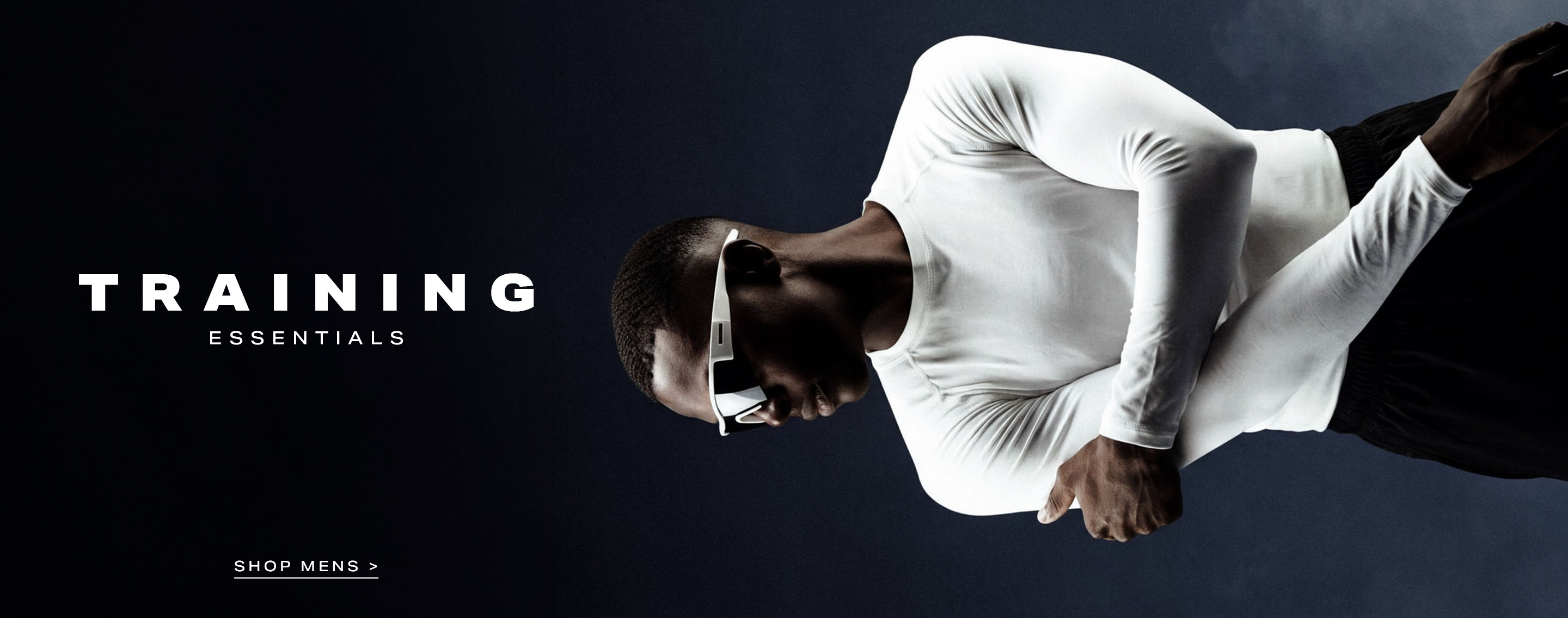 Man wearing a white compression shirt and sport sunglasses, arms crossed, against a dark background. Promotes men's training essentials and athletic apparel.