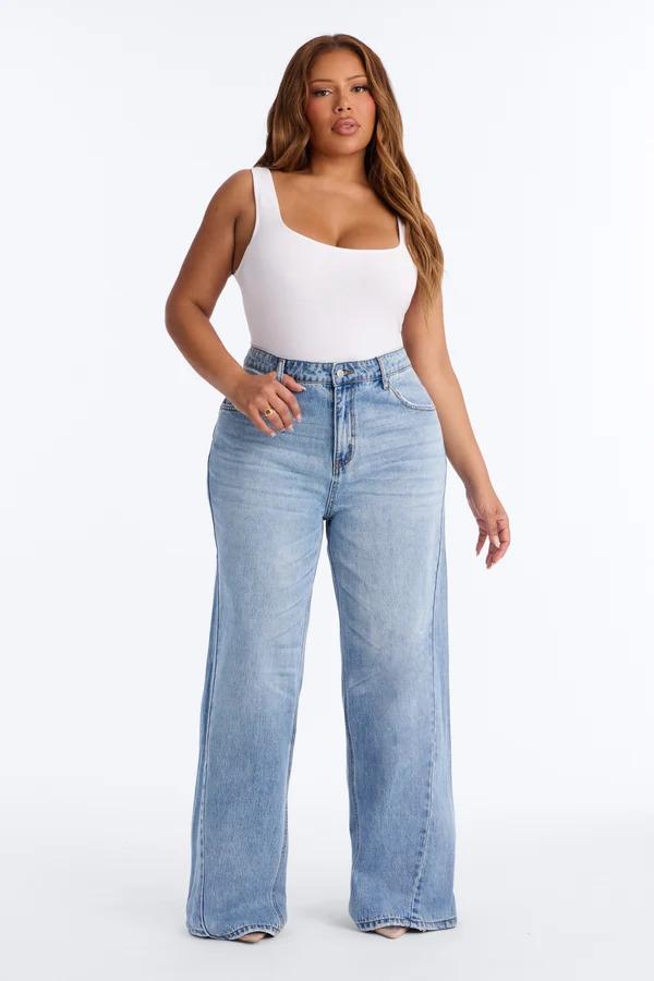 Modelo de talla grande posa con vaqueros de tiro alto y pierna ancha con un body blanco, destacando la moda denim curvy de tendencia.
