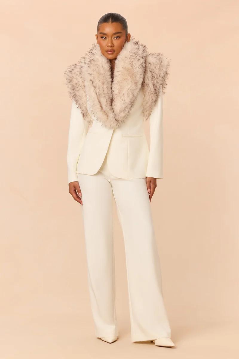 Model poses in a tailored cream white pantsuit featuring a plush faux fur collar shawl, showcasing luxury winter formal wear for women.