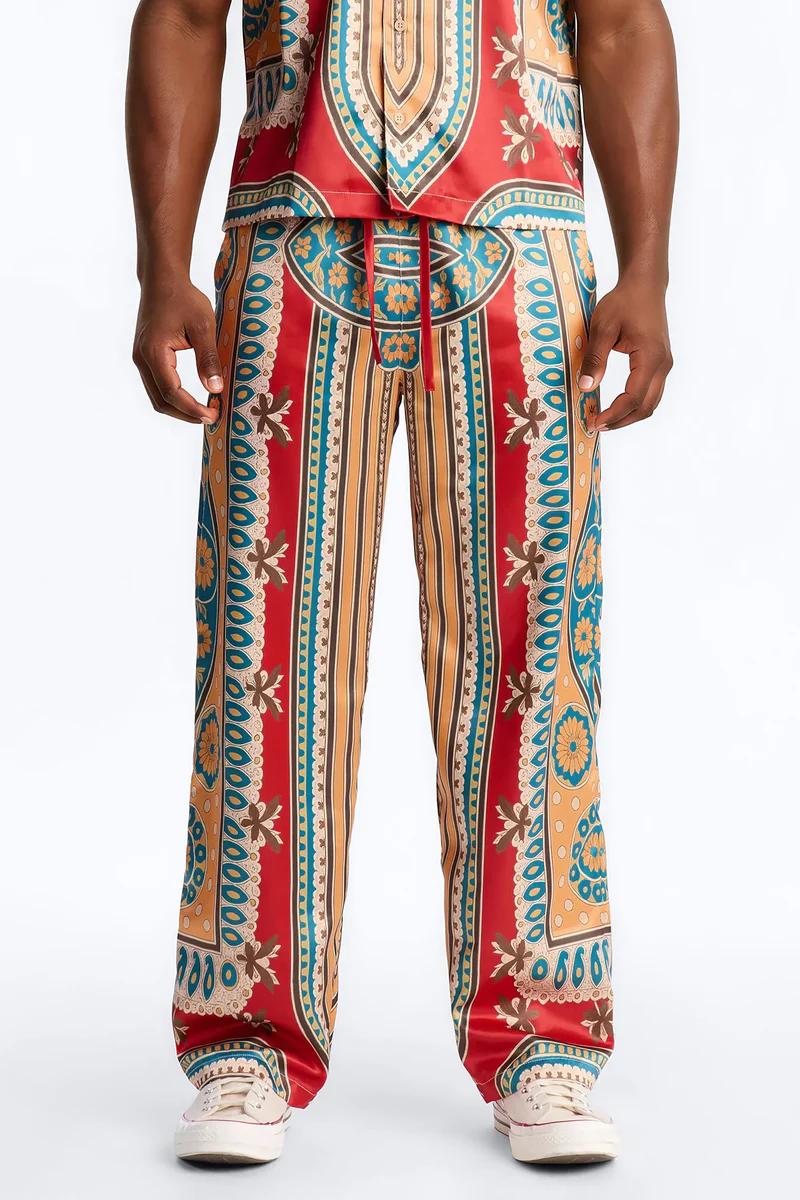 Hombre con pantalones palazzo y top a juego con estampado vibrante rojo, dorado y turquesa, mostrando una audaz nueva colección de moda.