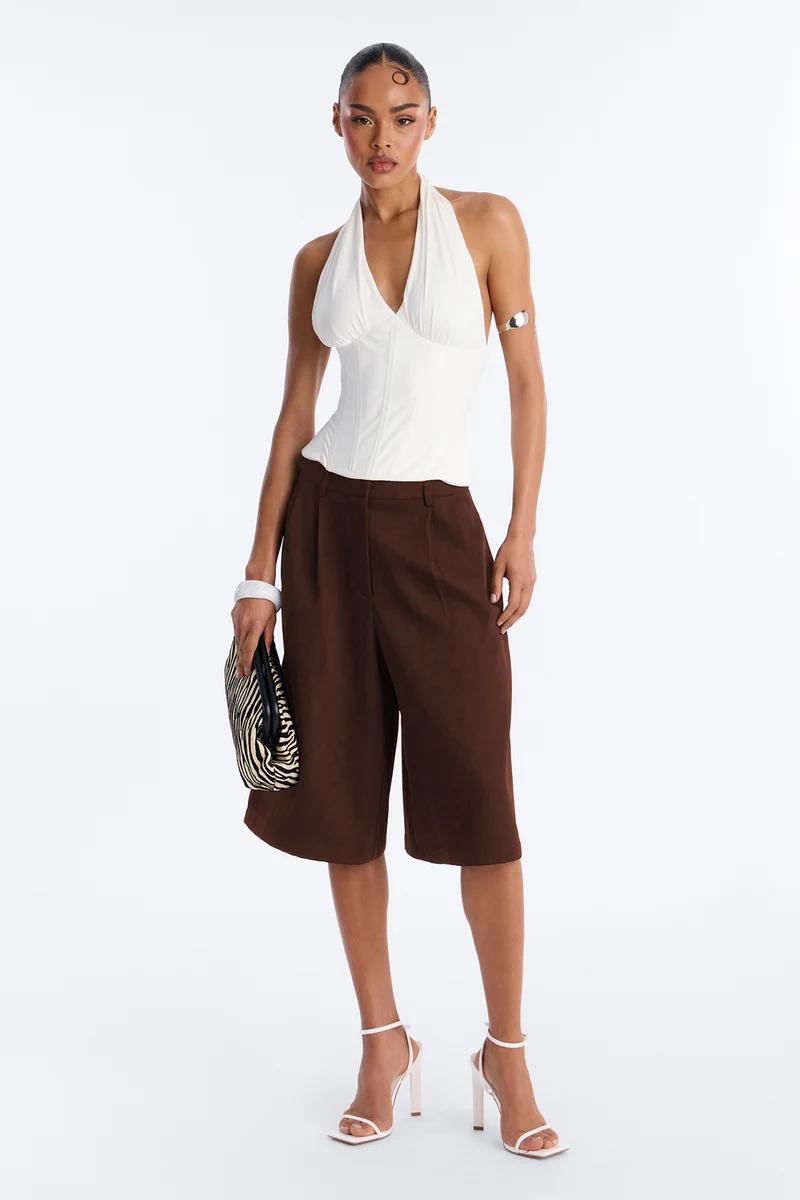 Woman wearing a white halter corset top and brown tailored bermuda shorts with white heels and a zebra print clutch.