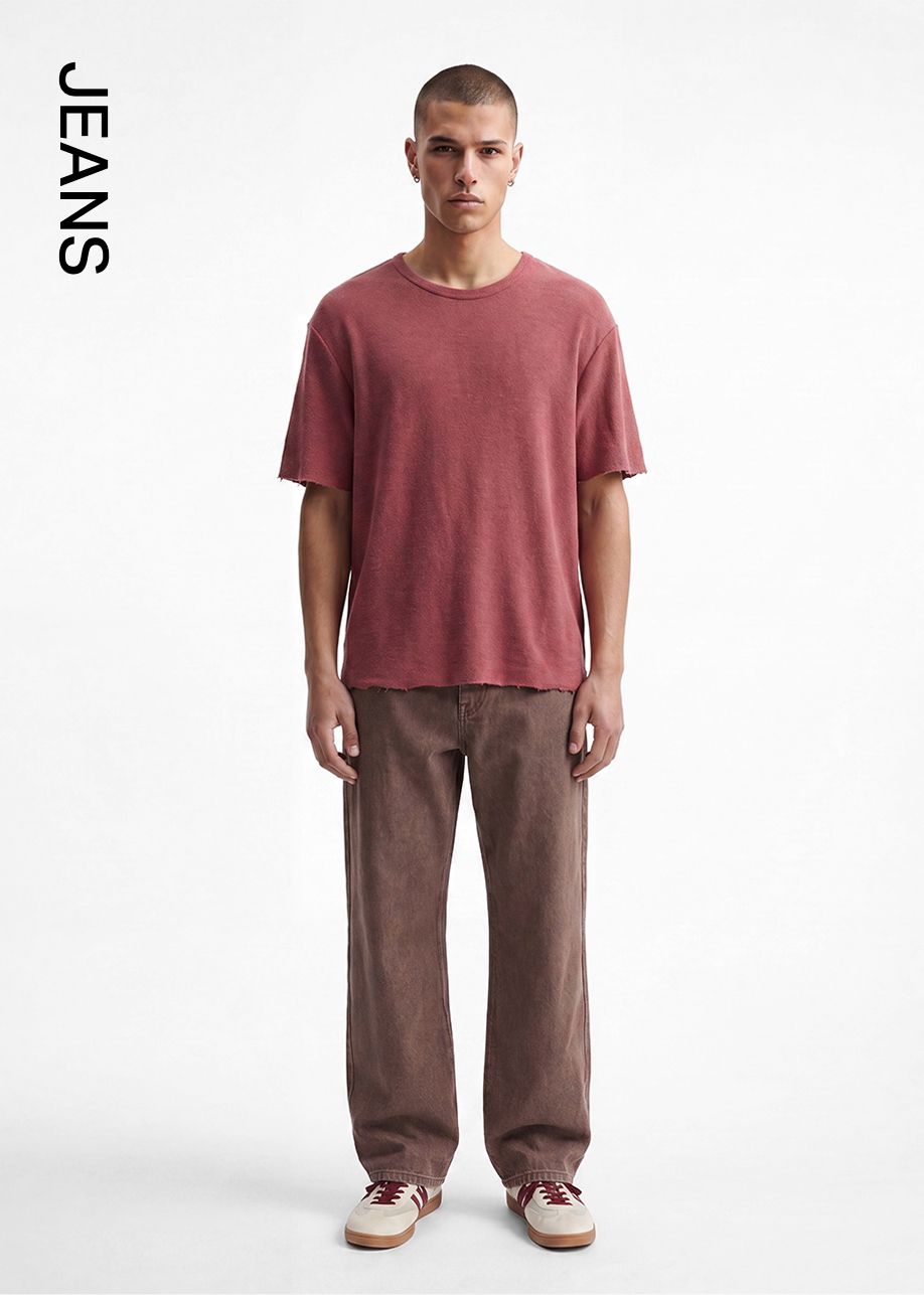 Hombre con camiseta marrón rojizo y jeans marrones de corte recto, mostrando un atuendo casual masculino con zapatillas. ¡Compra jeans!
