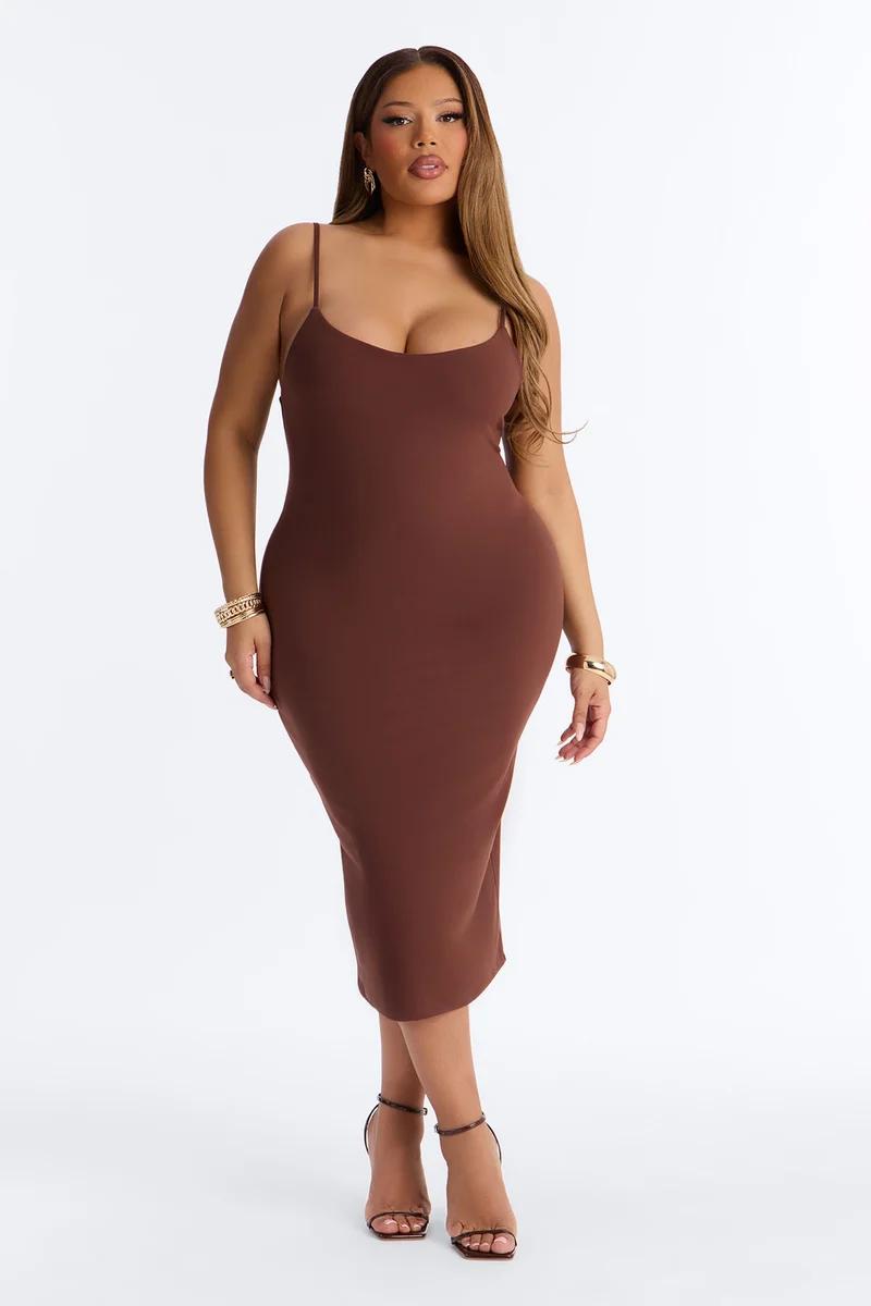 Curvy model showcasing a brown spaghetti-strap bodycon midi dress for a trendy fashion collection, posing against a white background.