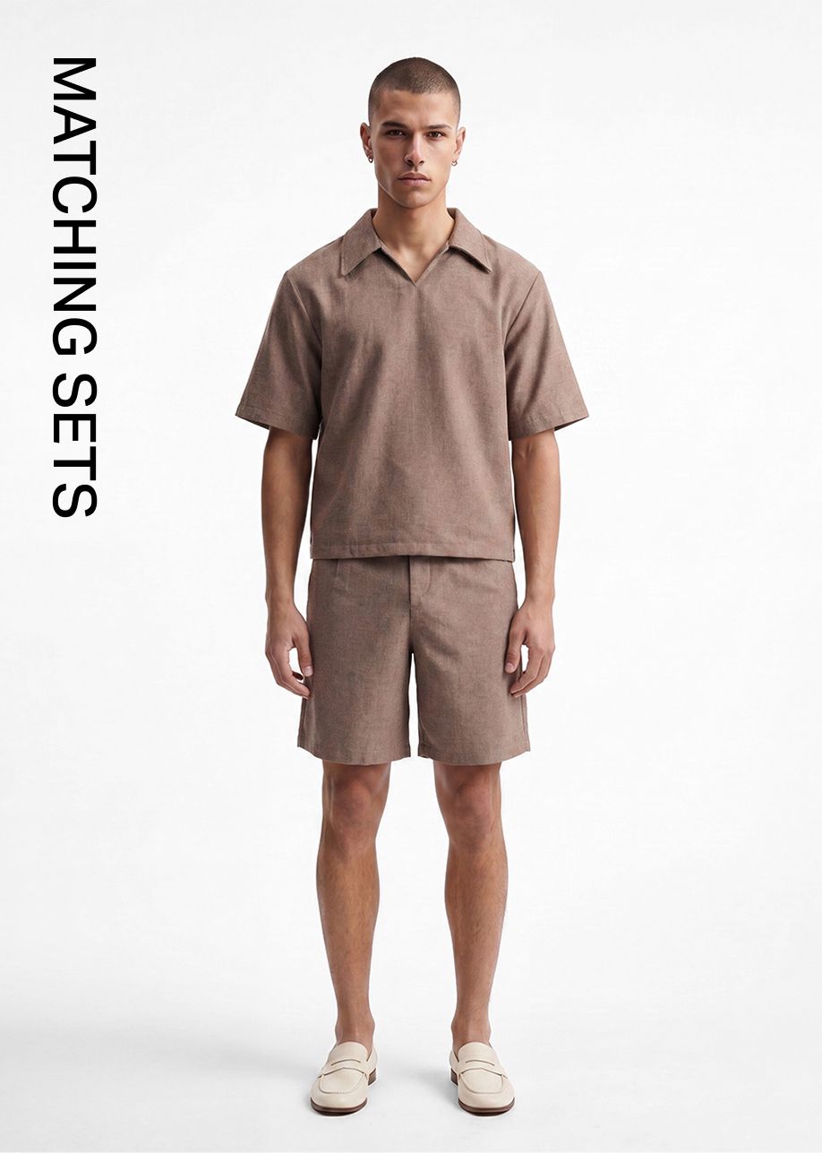 Male model in a brown short-sleeve collared shirt and matching shorts, with cream loafers. Promoting men's casual matching sets.