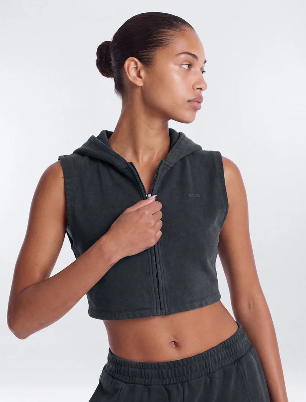 Woman wearing a dark grey cropped sleeveless zip-up hoodie and matching sweatpants, showcasing the new sporty activewear collection.
