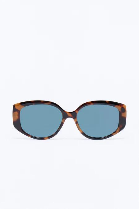 Elegantes gafas de sol rectangulares de carey con lentes azul claro brillantes, destacadas y centradas sobre un fondo blanco limpio.