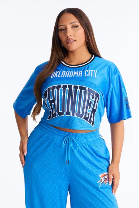 Mujer en top corto de malla azul rey con texto "Oklahoma City Thunder" y pantalones deportivos a juego, sobre fondo blanco.