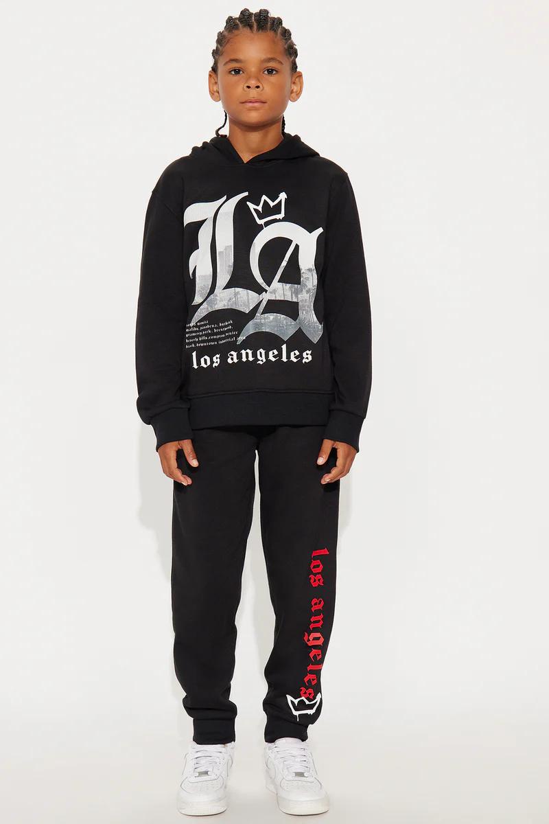 Young boy in black LA Los Angeles hoodie and sweatpants set, city graphic & crown. Kids' urban streetwear fashion.
