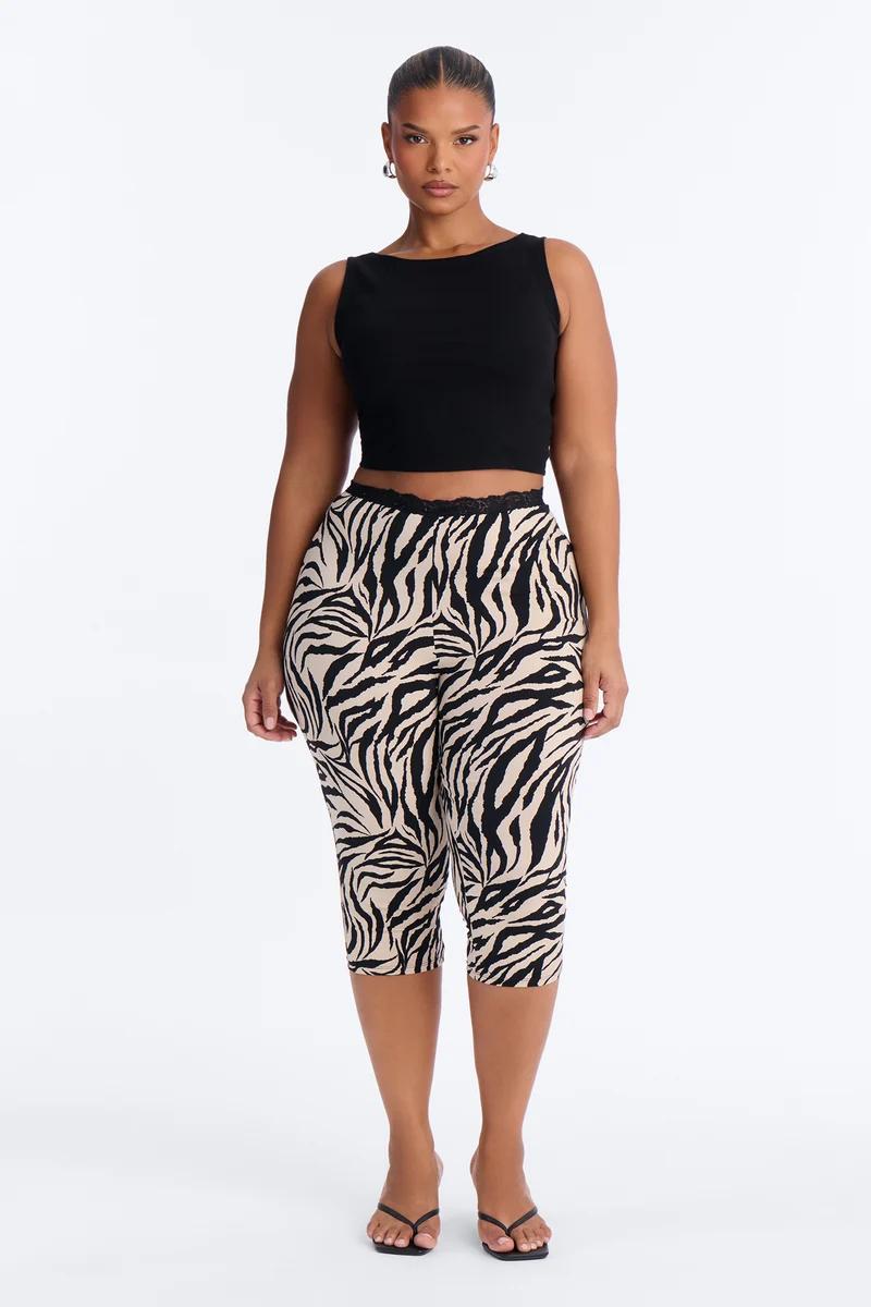 Modelo de talla grande posa con un top corto negro y leggings capri con estampado de cebra para promover la nueva colección de moda.