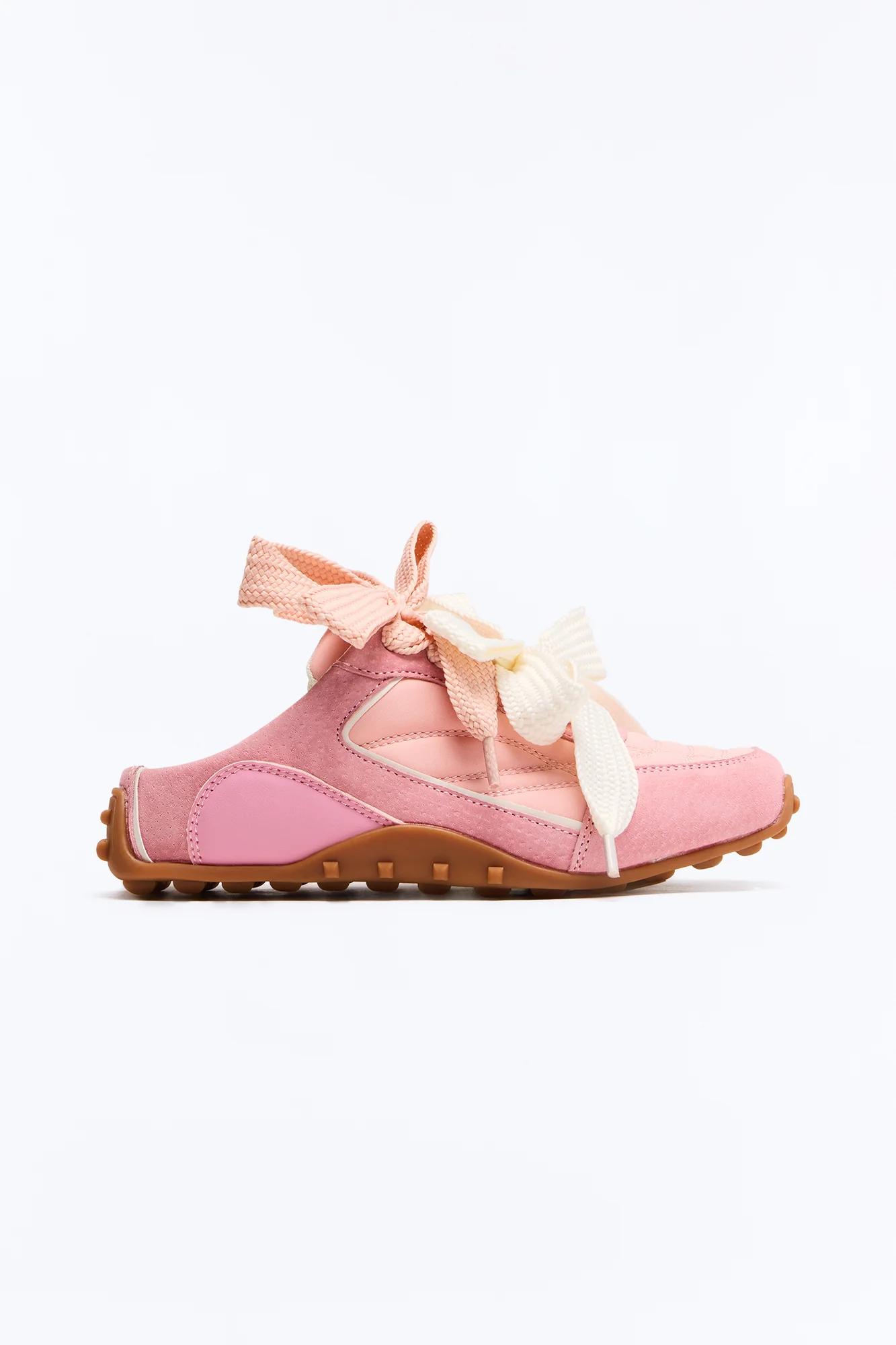 Pink suede and leather sneaker-style mule with cream laces tied in a bow, brown studded rubber sole, seen from the side.