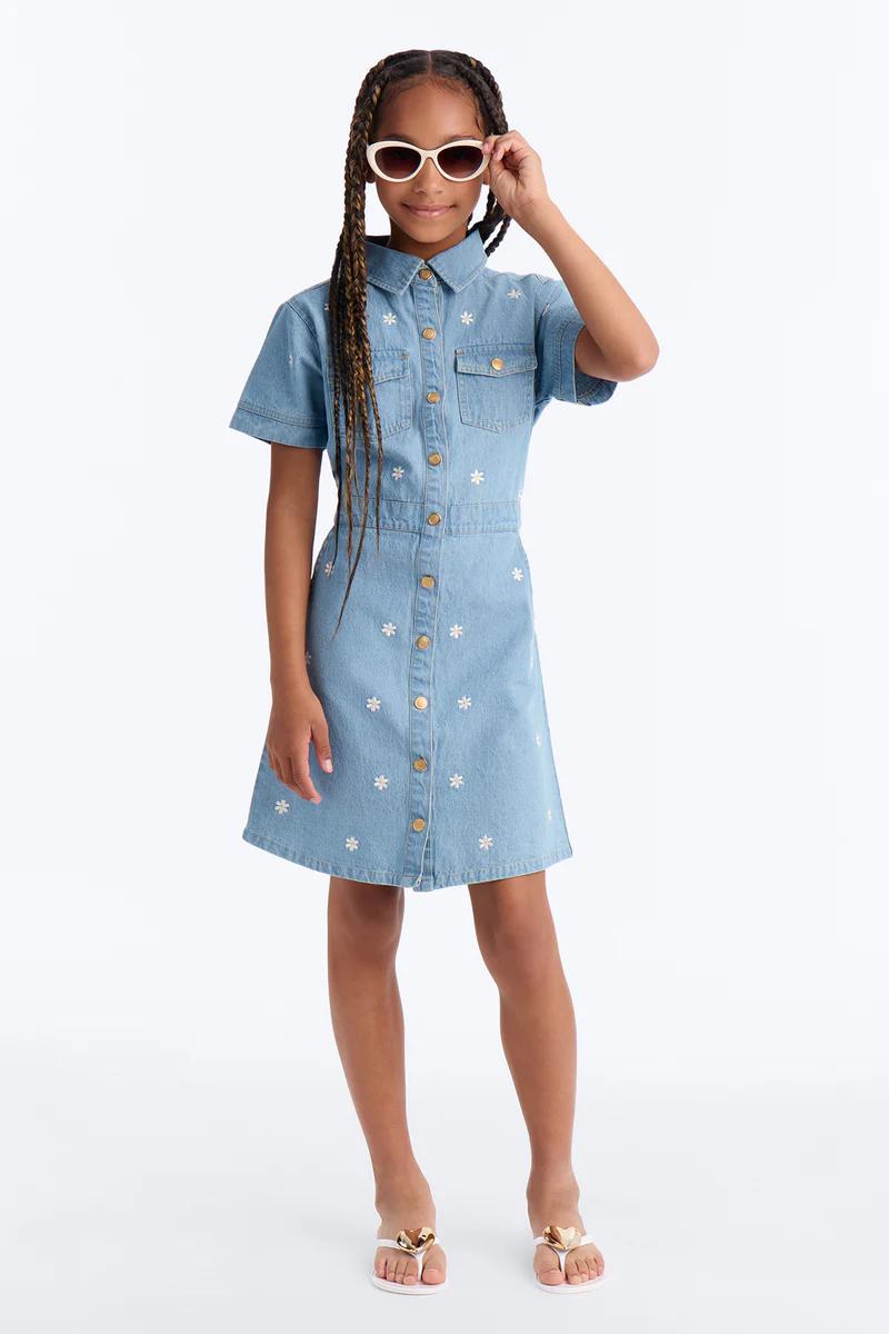 Niña con vestido vaquero azul claro de margaritas, gafas de sol cat-eye blancas y chanclas de corazón dorado. Vestido floral infantil.