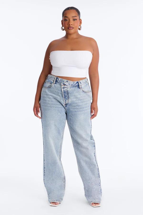 Modelo de talla grande con top de tubo blanco y jeans cruzados de pierna ancha y lavado claro, destacando moda curvy moderna.
