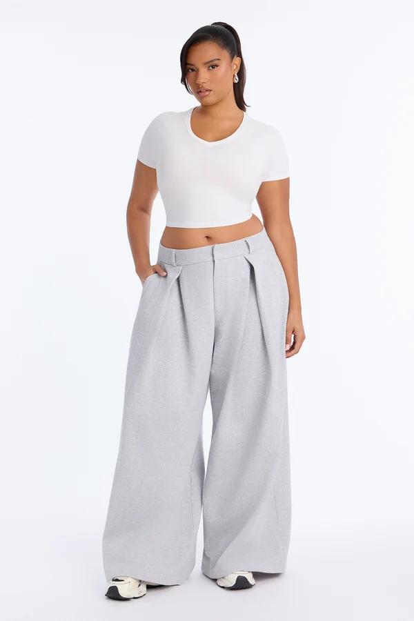 Woman in a white crop top and grey wide-leg pleated trousers showcasing a casual chic loungewear style against a white background.