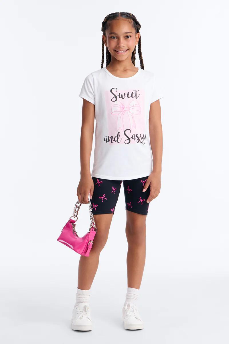 Young girl in "Sweet and Sassy" tee, black bow shorts, & pink handbag.