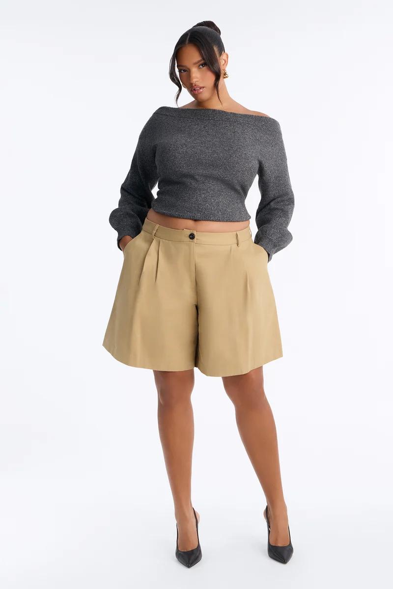 Modelo posando con suéter gris de hombros descubiertos y shorts plisados caqui, luciendo un estilo elegante para la moda de otoño.