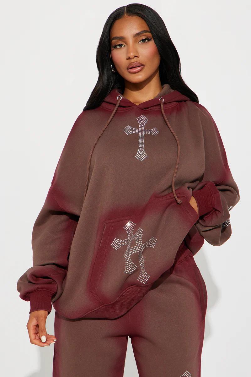 Woman in an oversized brown ombre rhinestone cross hoodie and matching sweatpants set.