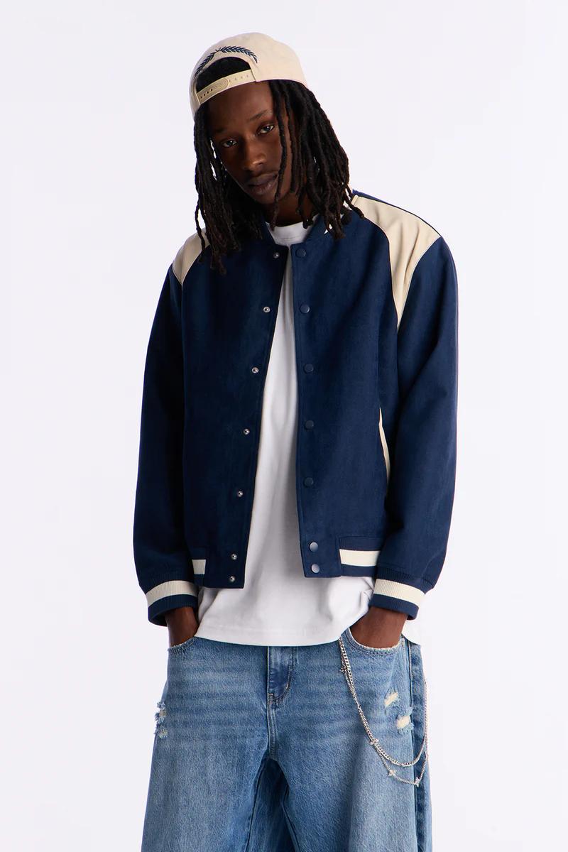 Stylish person in a navy blue and beige bomber jacket, distressed jeans, and cap. Showcasing new men's casual streetwear collection.